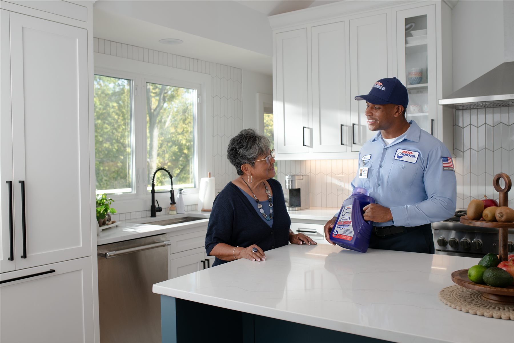 A Roto-Rooter technician handing a product to a customer across a kitchen counter