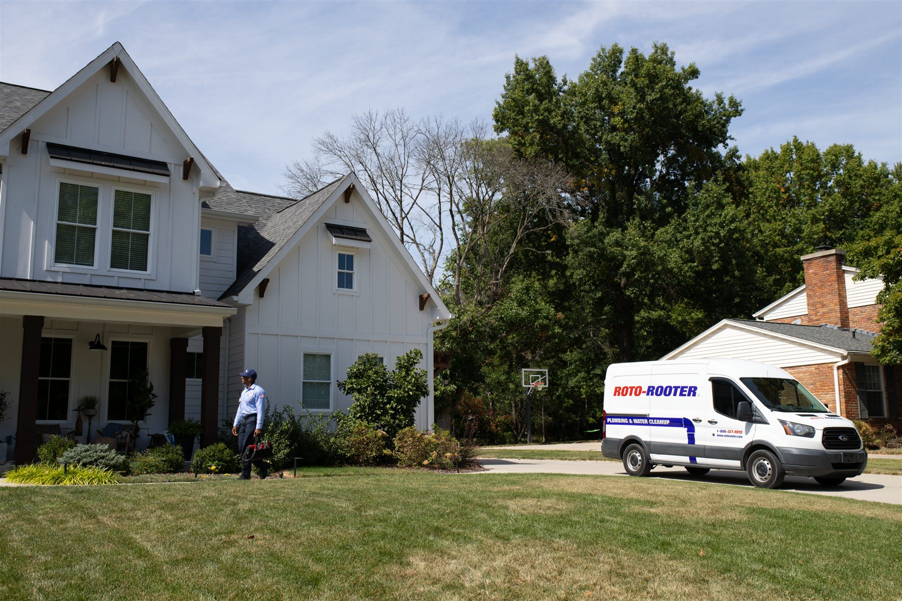 A Roto-Rooter technician walking toward a house, with a company van parked in the driveway.